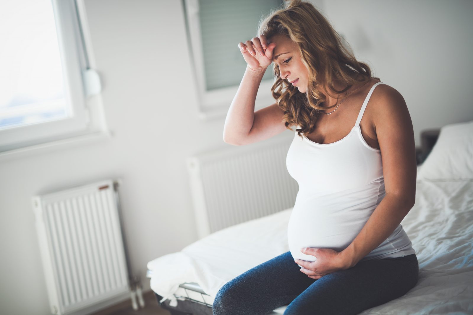 Trött gravid kvinna sitter på sängkanten