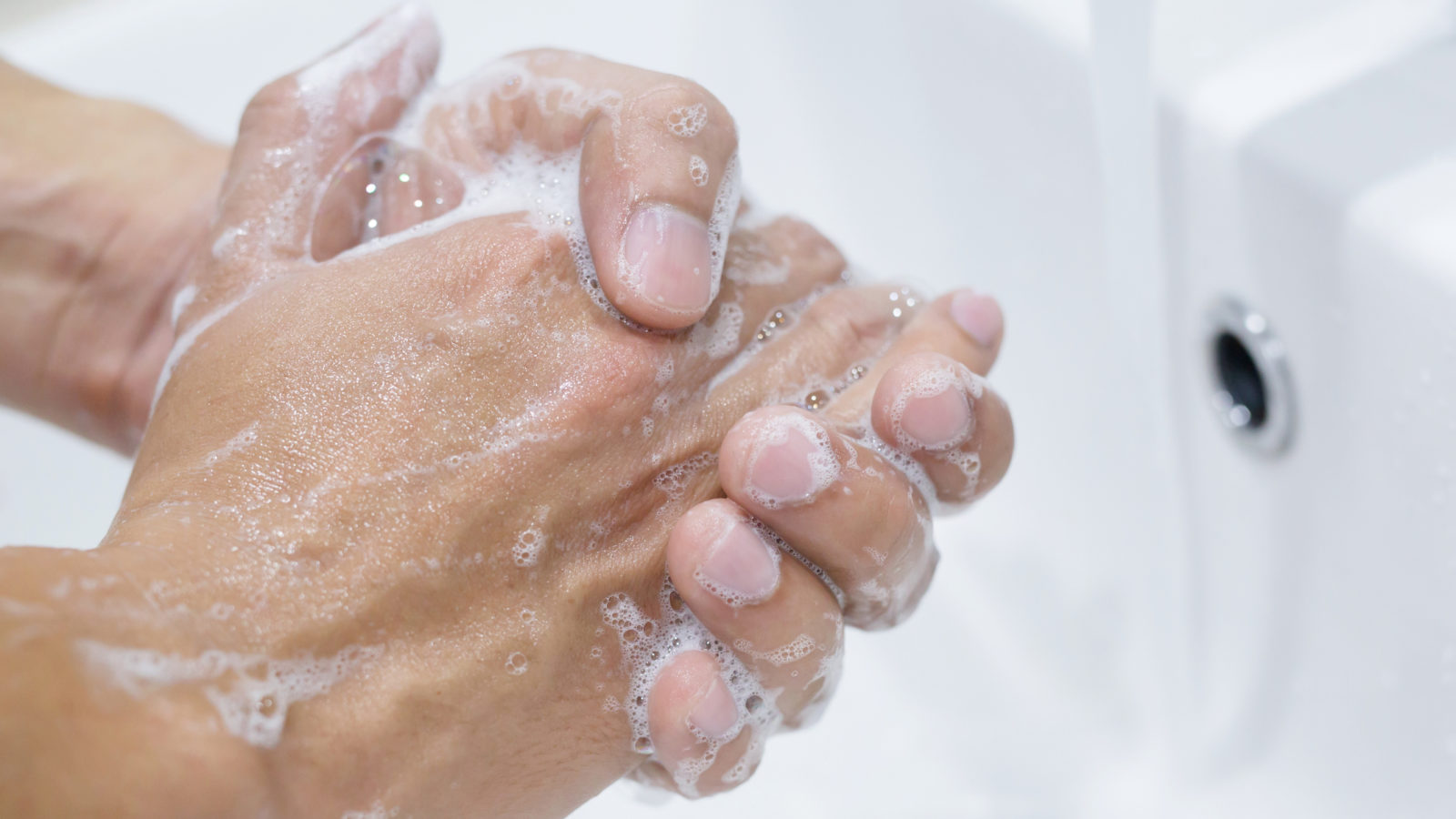 Händer tvättas i handfat under rinnande vatten